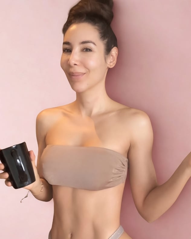 Mujer con top bandeau neutro sosteniendo un producto cosmético negro sobre fondo rosa, imagen del Reto 30 Días Desinflama de Caro Madrid